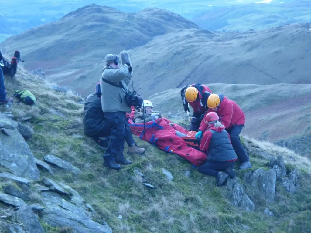 Team members treating a casualty on a stretcher on a rocky fellside