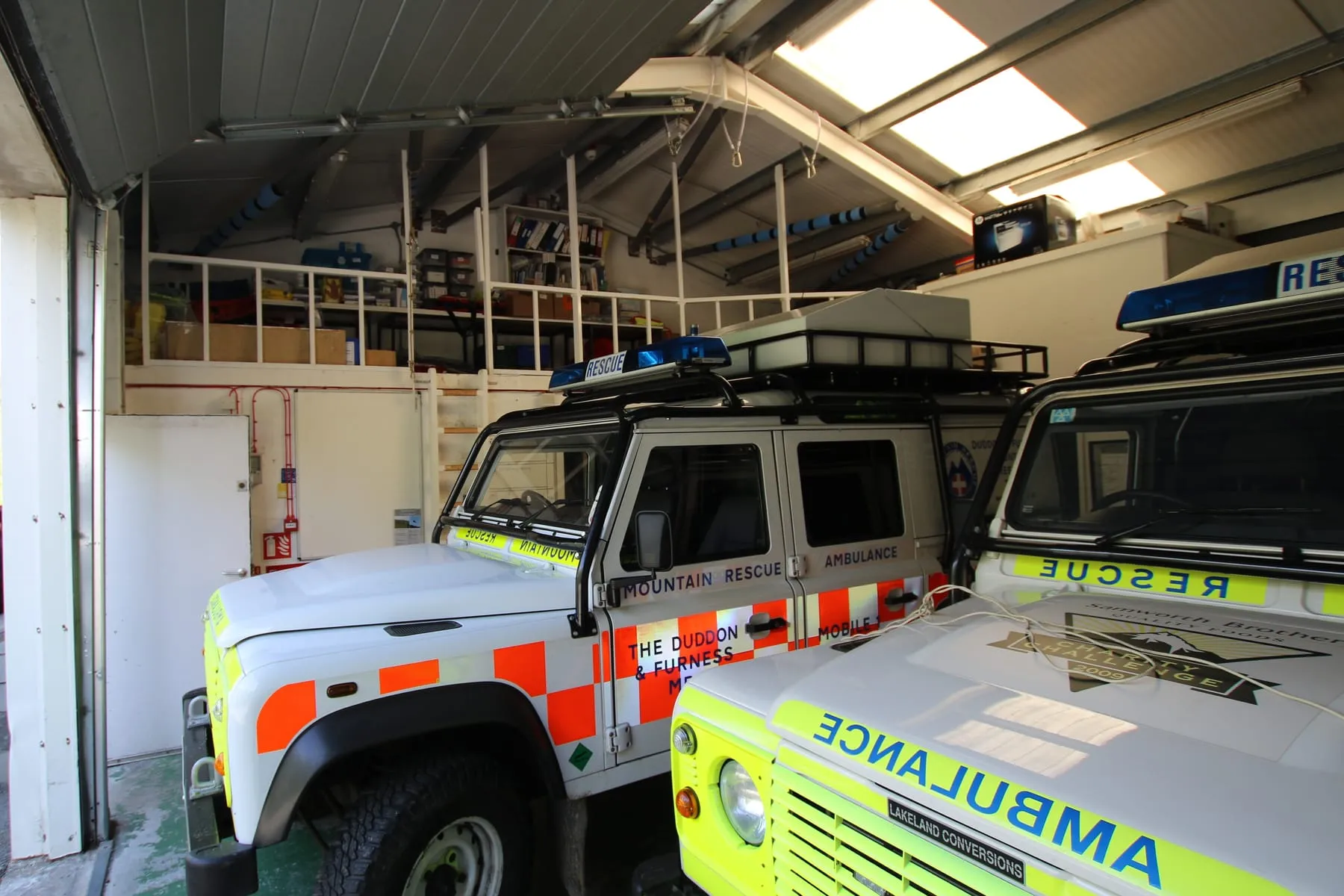 Two team vehicles parked inside the current base beneath a storage mezzanine