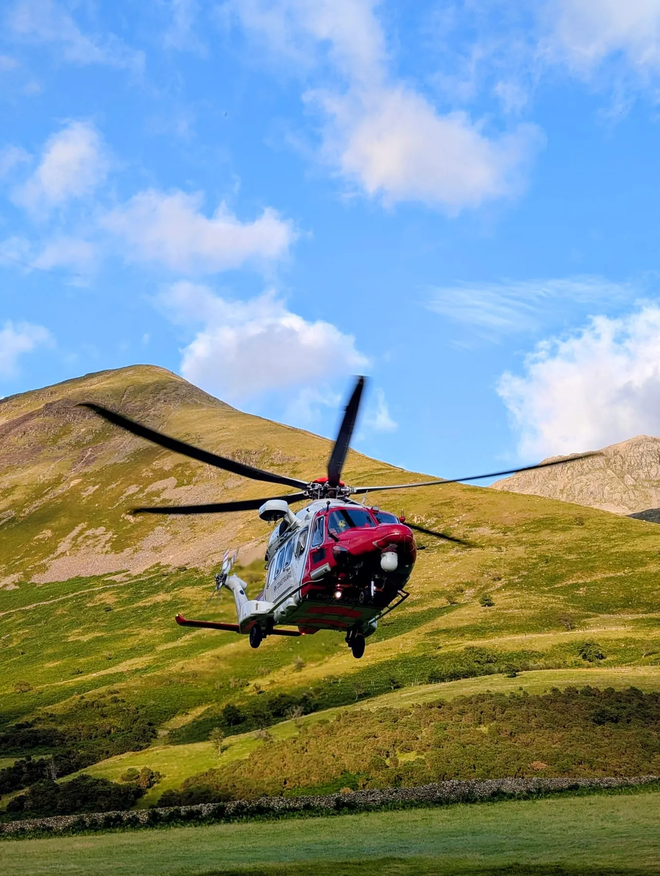 A red and white helicopter landing on a fellside