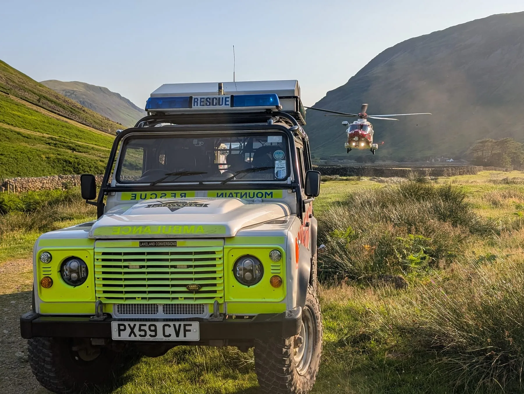 A team Land Rover with a helicopter landing behind it in a valley