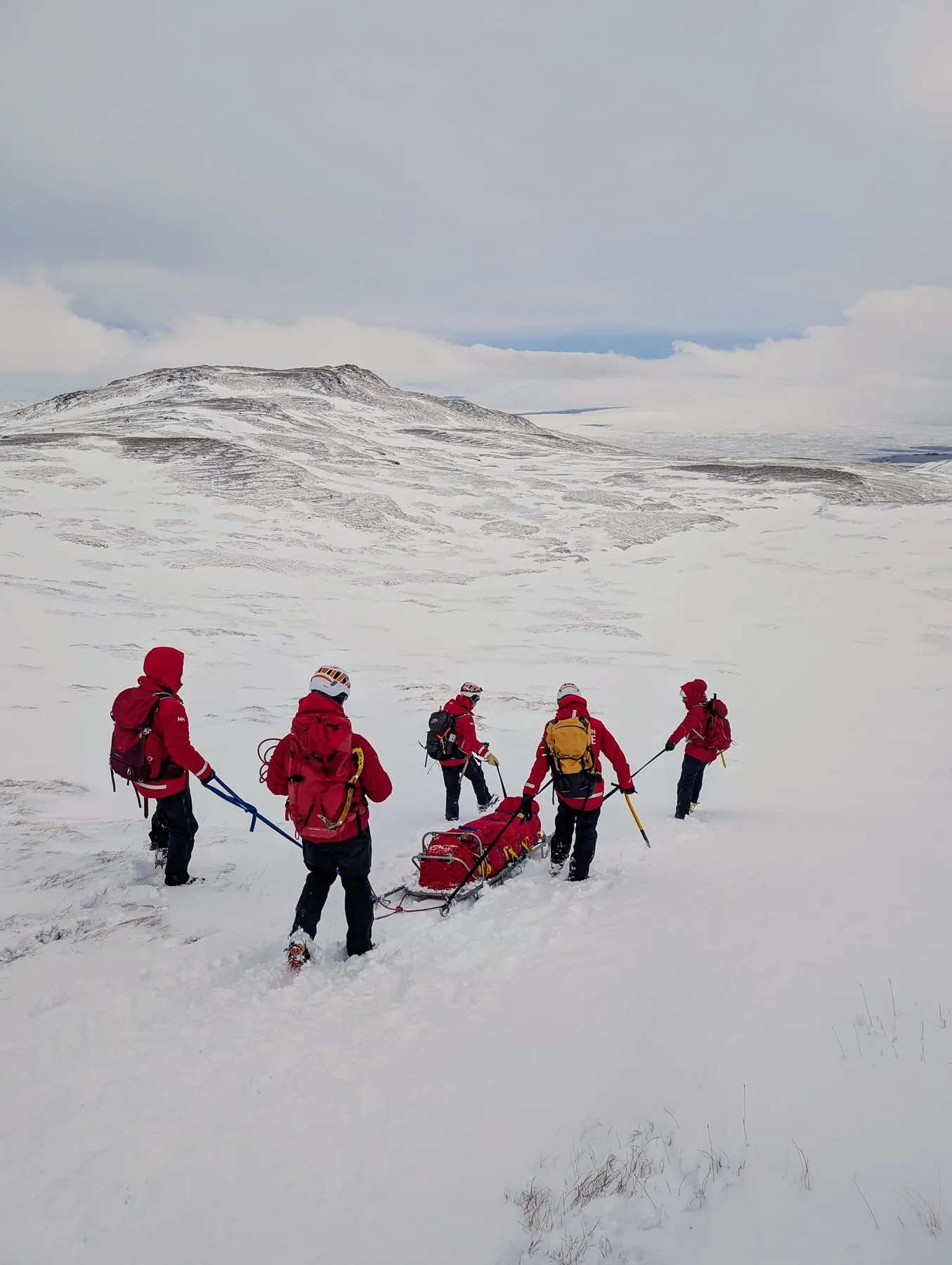 Team members hauling a stretcher across snow-covered fells
