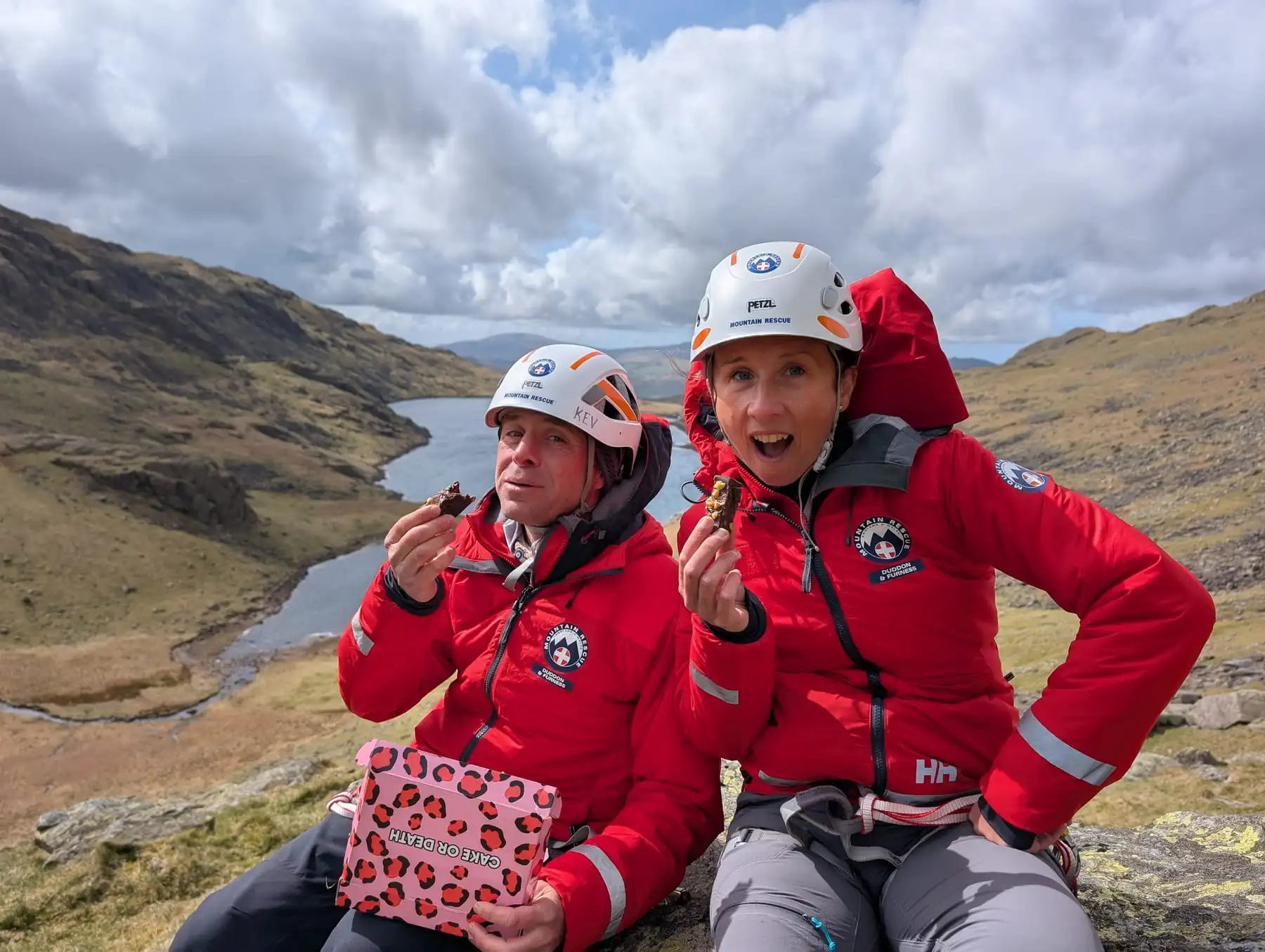 Two team members in helmets taking a break above a tarn
