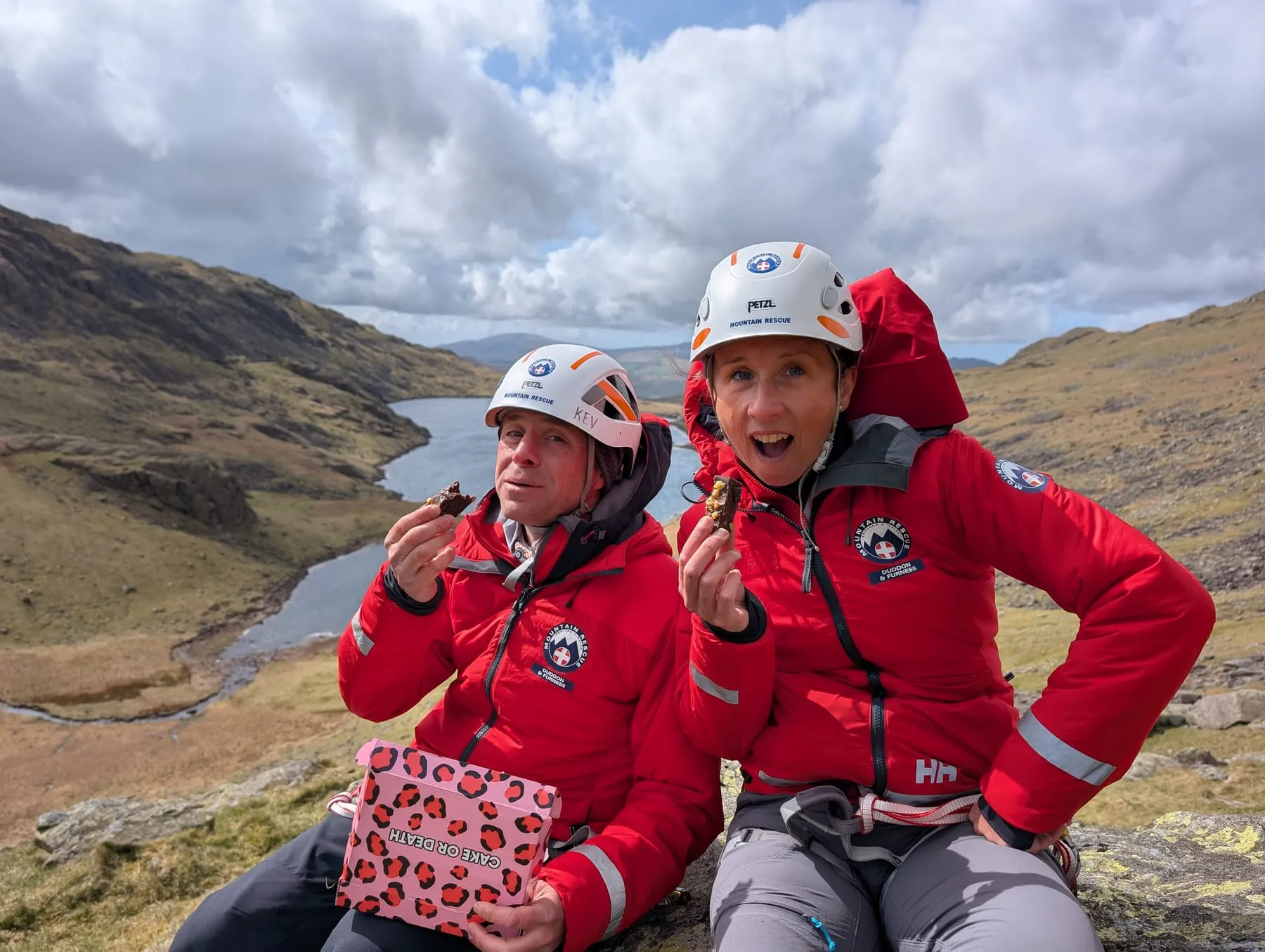 Two team members in helmets taking a break above a tarn